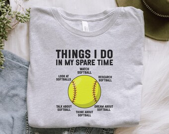 May include: Light gray t-shirt with the text "THINGS I DO IN MY SPARE TIME" above a yellow softball graphic. The graphic includes text such as "Watch Softball" and "Dream About Softball".