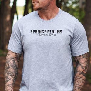 Pode incluir: Uma camiseta cinza com texto preto que diz "SPRINGFIELD, MO 37.21698° N 93.2924° W".