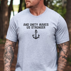 Puede incluir: Una camiseta gris con el texto "AND UNITY MAKES US STRONGER" y un gráfico de ancla.