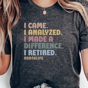 Könnte beinhalten: Dunkelgraues T-Shirt mit dem Text "I CAME. I ANALYZED. I MADE A DIFFERENCE. I RETIRED." in bunten Buchstaben. Der Hashtag #DATALIFE steht darunter. Ein lässiges Kleidungsstück.