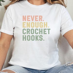 May include: A white t-shirt with the text "NEVER. ENOUGH. CROCHET HOOKS." printed in pink, yellow, and green.