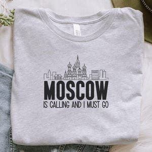 Może przedstawiać: Szary T-shirt z czarnym nadrukiem panoramy Moskwy i tekstem "Moskwa wzywa i muszę iść."