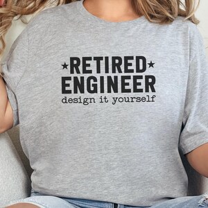 May include: A light gray t-shirt with the text "RETIRED ENGINEER design it yourself" in black. The text is centered on the shirt, with the word "RETIRED" above "ENGINEER". The shirt is short-sleeved.