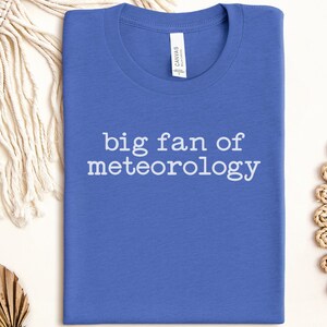 May include: A blue t-shirt with the text "big fan of meteorology" in white. The shirt is made of a soft material and is folded neatly. The shirt is a casual wear item.