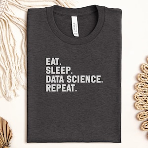 Könnte beinhalten: Dunkelgraues T-Shirt mit dem weißen Aufdruck „EAT. SLEEP. DATA SCIENCE. REPEAT.“. Das T-Shirt ist sauber gefaltet und hat einen Rundhalsausschnitt. Das T-Shirt ist aus einem weichen Material.
