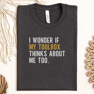 May include: Dark gray t-shirt with the text "I wonder if my toolbox thinks about me too." printed in white with the word "toolbox" in gold.