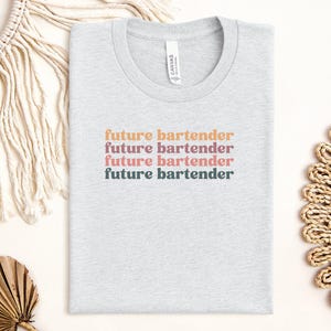 May include: A gray t-shirt with the text "future bartender" repeated four times in different colors. The text is in a retro font style.