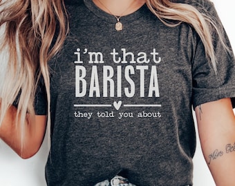 May include: Dark gray t-shirt with the text "i'm that BARISTA they told you about" in white. The shirt has a crew neck and short sleeves. A small heart is between the words "BARISTA" and "they".