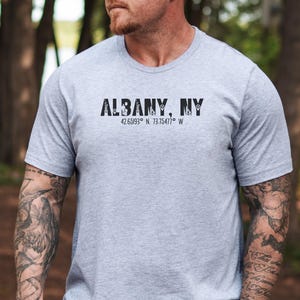 May include: A gray t-shirt with the text "ALBANY, NY" and the coordinates "42.65193° N, 73.75477° W" printed on the front.