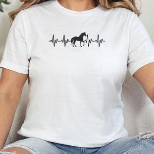 Puede incluir: Camiseta blanca con una silueta negra de un caballo y un gráfico de latido del corazón. El gráfico dice "My Heart Beats for Horses".
