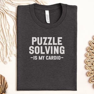May include: Dark gray t-shirt with white text that reads "Puzzle Solving - Is My Cardio - "