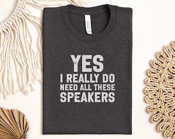 May include: Dark gray t-shirt with the text "YES I REALLY DO NEED ALL THESE SPEAKERS" in distressed white lettering. The shirt is folded neatly and has a tag that says "CANVAS".