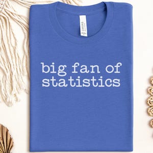 May include: A blue t-shirt with the white text "big fan of statistics". The shirt is folded and centered. The image shows a close-up of the shirt, highlighting the text and the fabric's texture.