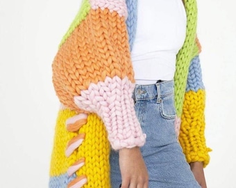 May include: A long, colorful knitted cardigan with a patchwork design in shades of pink, orange, yellow, blue, and green. The cardigan has a relaxed fit and a loose, oversized silhouette.