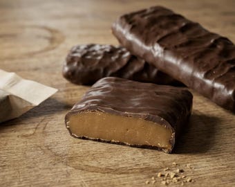 May include: Three rectangular chocolate-covered confections with a smooth, light brown interior filling. One piece is sliced in half to reveal the dense, tan-colored center, while the other two remain whole and coated in a dark, rippled chocolate shell.