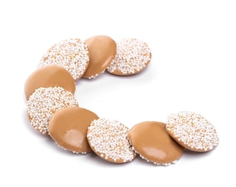 May include: A close-up of a group of round, milk chocolate candies with white sprinkles. The candies are arranged in a semi-circle on a white background.