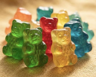 May include: A collection of translucent gummy candies shaped like small bears in various vibrant colors including red, green, yellow, orange, and blue. Each bear features a molded face with ears, eyes, and a nose, along with visible paw details.