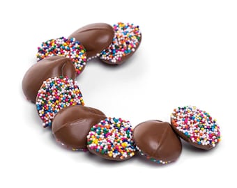 May include: Oval-shaped chocolate candies, some covered in colorful sprinkles, arranged in a curved pattern. The candies are a rich brown color, with the sprinkles adding a vibrant contrast. A sweet treat.