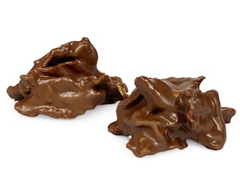 May include: Two pieces of chocolate peanut brittle, a popular sweet treat, are shown on a white background. The brittle is made with peanuts and milk chocolate.