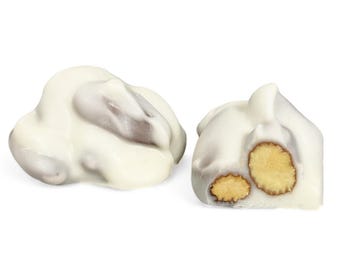 May include: Two pieces of white chocolate-covered candy. One piece is a rounded shape, and the other is cut to reveal a light brown nut. The candy has a smooth, glossy appearance.