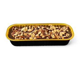 May include: A rectangular chocolate dessert in a black and gold foil container. The dessert is topped with chopped almonds. The container is sitting on a white surface.