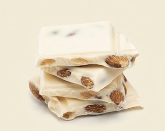 May include: A stack of four rectangular white chocolate squares featuring visible whole brown almonds embedded throughout the smooth, creamy surface. The pieces are layered unevenly, showcasing the contrast between the pale chocolate and nuts.