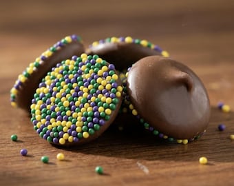 Könnte beinhalten: Eine Ansammlung runder Schokoladenbonbons, einige mit glatter brauner Oberfläche und andere mit kleinen, kugelförmigen Streuseln in Violett, Grün und Gelb bedeckt. Die Bonbons sind in einem kleinen Haufen angeordnet, wobei einige Streusel verstreut sind.