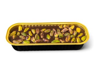 May include: A rectangular dessert in a black and gold container. The dessert is a dark chocolate base topped with a generous scattering of green and brown pistachios. The container has a gold rim and a black exterior.