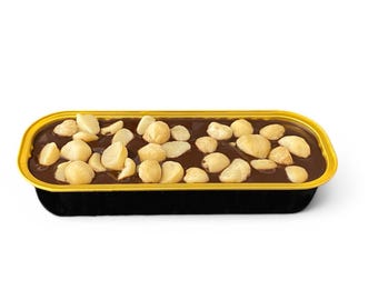 May include: A rectangular dessert in a black container with a gold rim. The dessert has a dark brown, glossy surface, generously topped with light-colored macadamia nuts. The overall presentation suggests a rich, decadent treat.