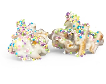 May include: White chocolate pretzels covered in colorful sprinkles. The pretzels are arranged in a pile on a white background.
