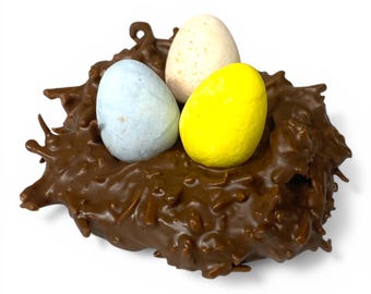 May include: A chocolate nest with three speckled eggs. The eggs are pastel blue, pale yellow, and cream-colored. The nest is a rich, dark brown color and has a textured appearance. The image is set against a white background.