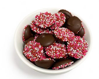 May include: A white bowl filled with chocolate covered candies. The candies are covered in pink and white sprinkles.