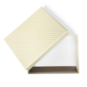 May include: A rectangular gift box with a cream-colored lid featuring a subtle, repeating diamond-shaped embossed texture. The base of the box is open, revealing a plain white interior and a solid cream-colored side wall structure.