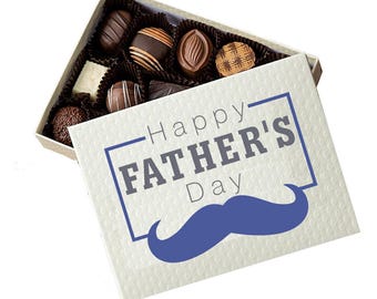 May include: A square gift box containing an assortment of dark and milk chocolates in paper liners. The lid is off-white with a textured diamond pattern and features the blue text Happy FATHER'S Day above a blue graphic of a mustache.