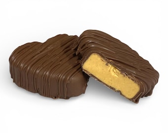 May include: Two chocolate-covered peanut butter candies, one heart-shaped and the other rectangular, sit on a white background. The rectangular candy is cut open, revealing a creamy peanut butter filling. The candies are drizzled with chocolate.
