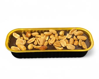 May include: A rectangular chocolate dessert topped with peanuts, presented in a gold-rimmed black container. The dessert has a rich, dark brown color, and the peanuts are scattered across the top.