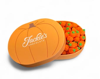 May include: An orange pumpkin-shaped box with the text "Jackie's Chocolate" in a cursive font. The box is open, revealing numerous small, orange pumpkin candies with green stems. The candies are in a light orange container.
