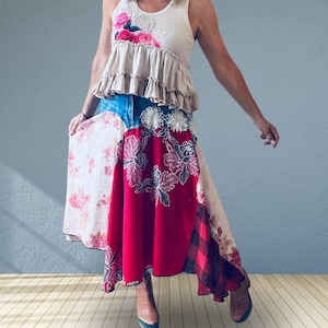 May include: A sleeveless beige tank top with a ruffled hem and pink floral accents paired with a long, multi-patterned skirt. The skirt features panels of red fabric with white floral embroidery, light floral prints, and a dark red plaid section.