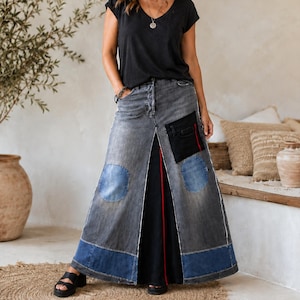 Op de afbeelding: Een zwart T-shirt met korte mouwen en V-hals gecombineerd met een lange spijkerrok. De rok heeft een vervaagde grijze wassing, een split aan de voorzijde, blauwe denim patches, een zwart zakje met een rode streep en een donkerblauwe zoom.