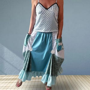 May include: A two-piece outfit consisting of a white camisole with black polka dots and a V-neckline, paired with a multi-paneled skirt featuring teal, white, and sage green floral patterns, side pockets, and a ruffled hemline with decorative accents.