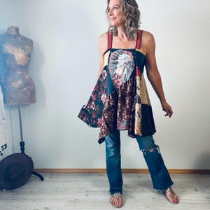 Puede incluir: Una túnica patchwork con un diseño de inspiración nativa americana, con una mezcla de telas florales y estampadas en tonos burdeos, marrón y beige. La parte superior tiene correas rojas y se combina con jeans azules.