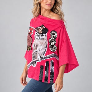 May include: A bright pink poncho-style top featuring a large owl illustration perched on a branch, accented with floral appliques, a butterfly, and black-and-white newspaper-print fabric strips at the hem, with a wide, off-the-shoulder neckline.