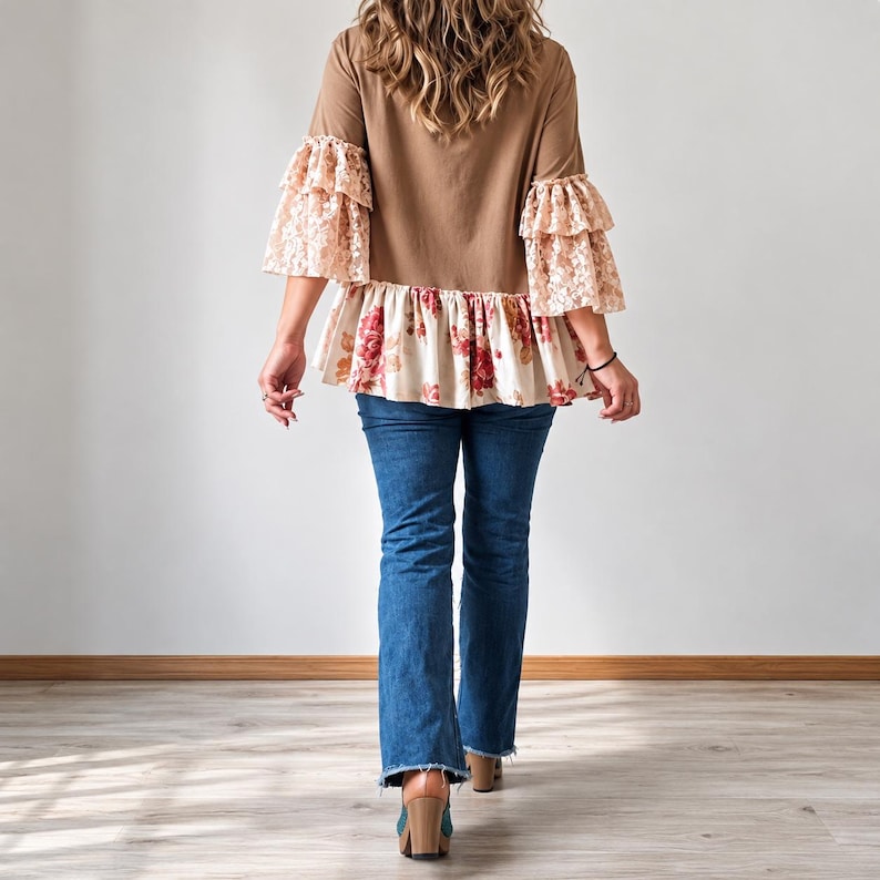 May include: A tan top featuring three-quarter length sleeves with double-layered lace ruffles and a flared hemline with a red and pink floral print. The garment is paired with blue denim jeans and tan heeled shoes, viewed from the back.