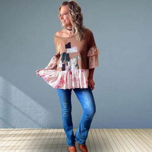 May include: A brown long-sleeve top featuring a patchwork design on the chest, lace-trimmed sleeves, and a ruffled hem with a pink floral pattern, paired with blue denim jeans and brown patterned shoes. The top has a wide neckline and loose fit.