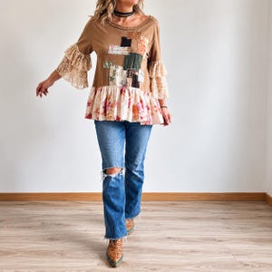 May include: A tan long-sleeve top featuring a patchwork design on the chest, tiered beige lace sleeves, and a floral print peplum hem, paired with blue denim jeans that have distressed knee detailing and brown leopard print pointed-toe boots.