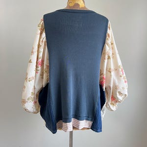 May include: A unique top with a navy blue bodice, denim panels, and floral print sleeves. The sleeves are a cream color with pink and brown floral patterns. The bottom hem features a pink and white striped detail.
