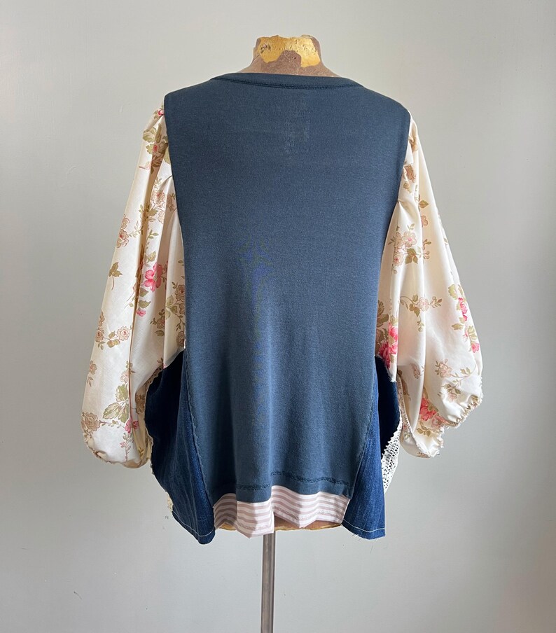 May include: A unique top with a navy blue bodice, denim panels, and floral print sleeves. The sleeves are a cream color with pink and brown floral patterns. The bottom hem features a pink and white striped detail.