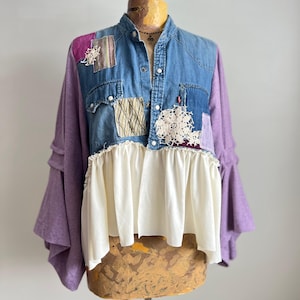 Puede incluir: Top de patchwork con corpiño de mezclilla, mangas moradas y dobladillo con volantes blancos. La mezclilla presenta parches decorativos y cierres a presión blancos. Las mangas son de color morado liso. La parte superior se muestra en un maniquí.