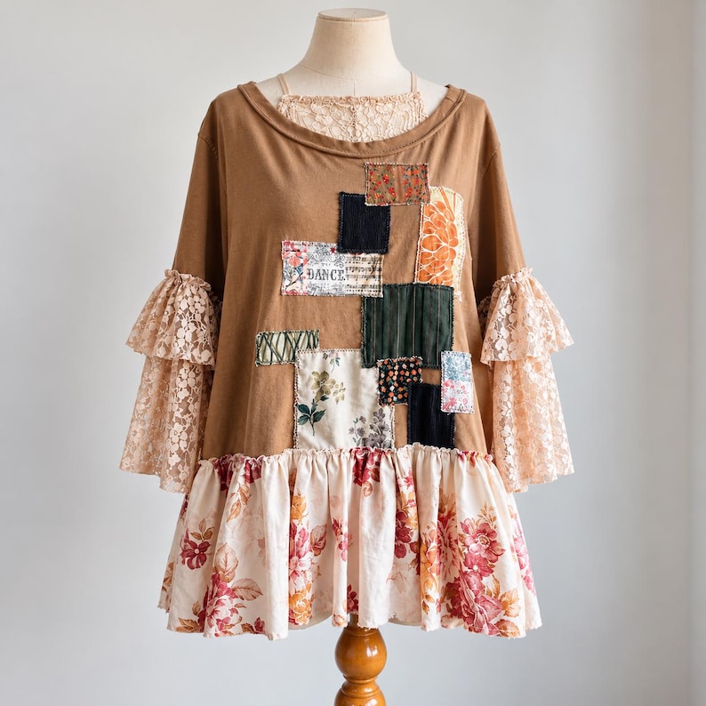May include: A brown long-sleeve top featuring a layered lace neckline, tiered lace sleeves, and a floral ruffled hem. The front is decorated with various rectangular fabric patches in floral, solid, and patterned designs, including one with the word DANCE.