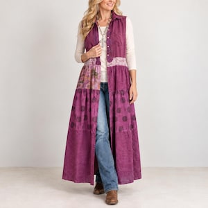May include: A long, sleeveless, button-down magenta vest featuring a tiered design with a polka dot pattern on the lower section, a floral print panel, and a lace-trimmed bodice. The vest is worn over a long-sleeve cream top and blue denim jeans.